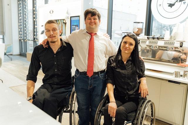 A young man with downs syndrome with his hands around the shoulders of a man and women in wheelchairs